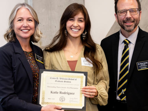 Three individuals smiling for a photo. The individual in the middle is holding a certificate.