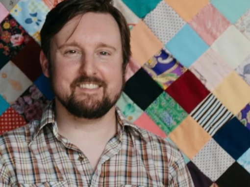 A man smiling next to a quilt.